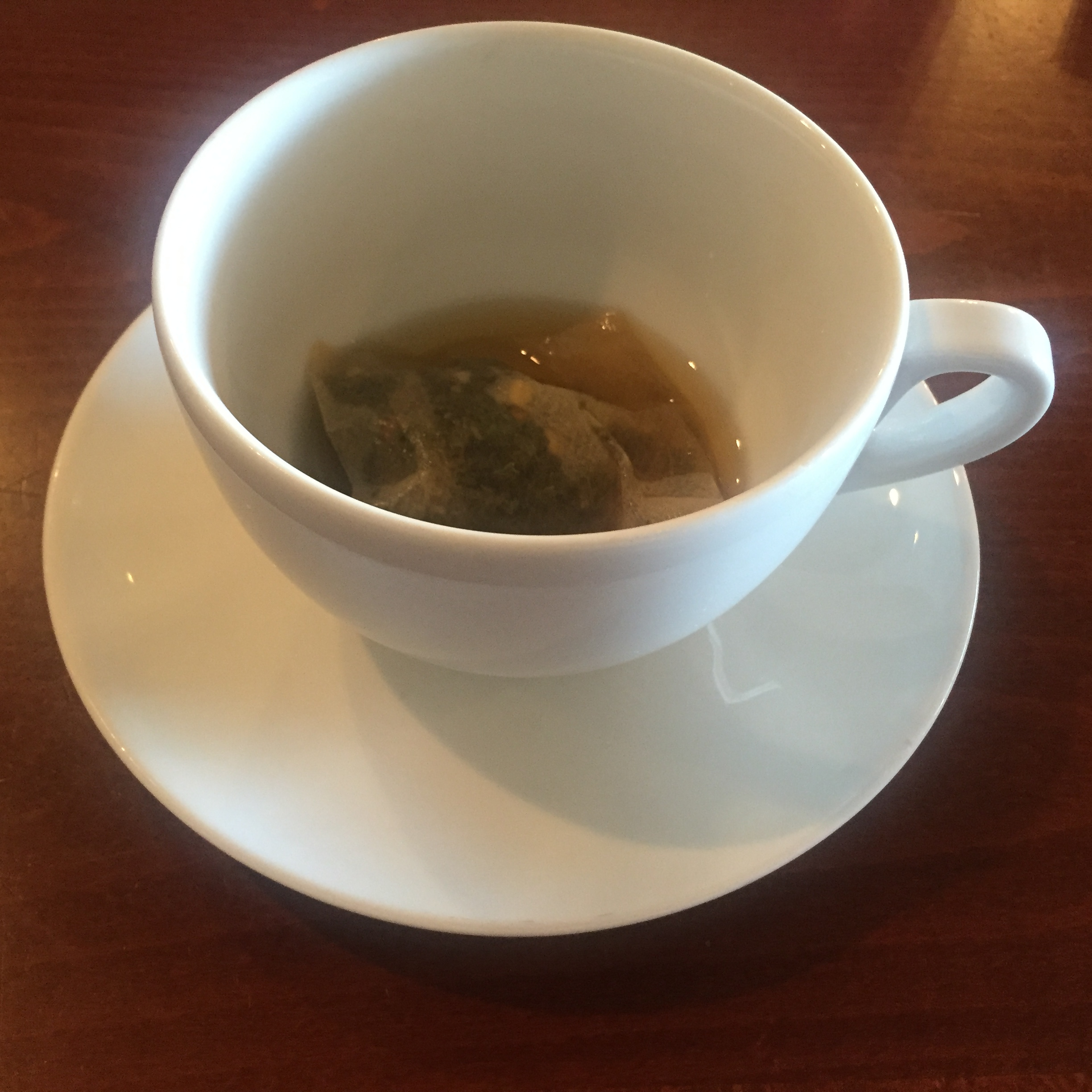 White tea cup with a tea bag and just a little tea left