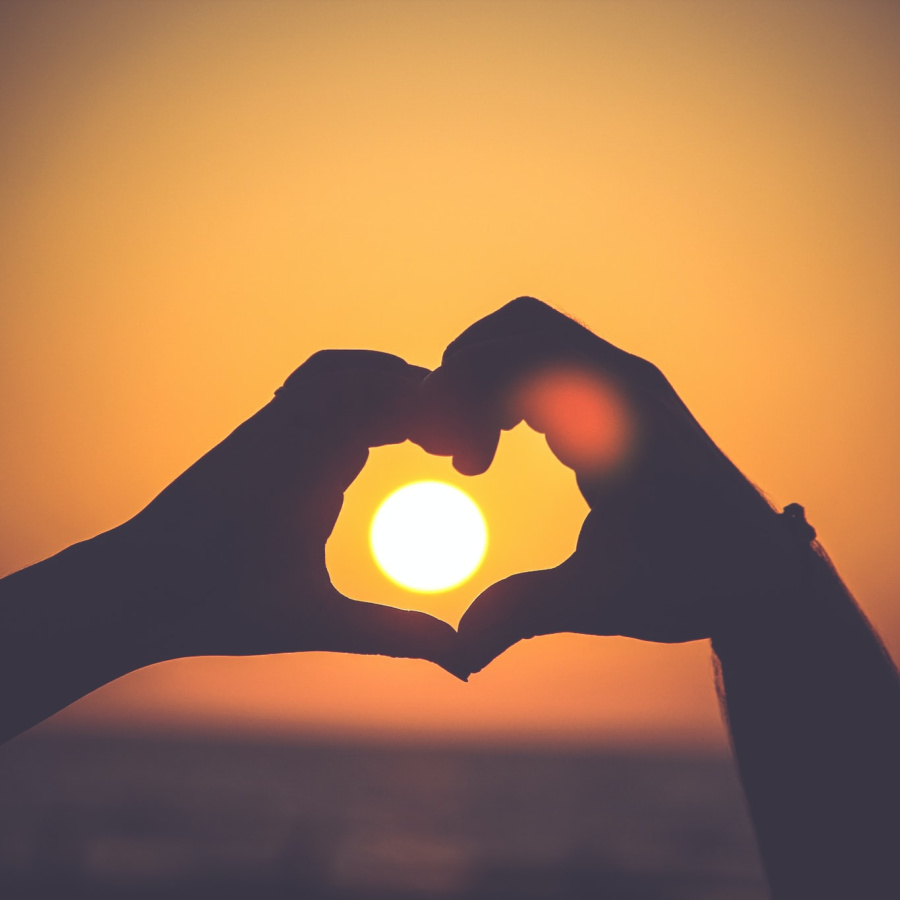 Image of hands forming a heart over a sun rising or setting