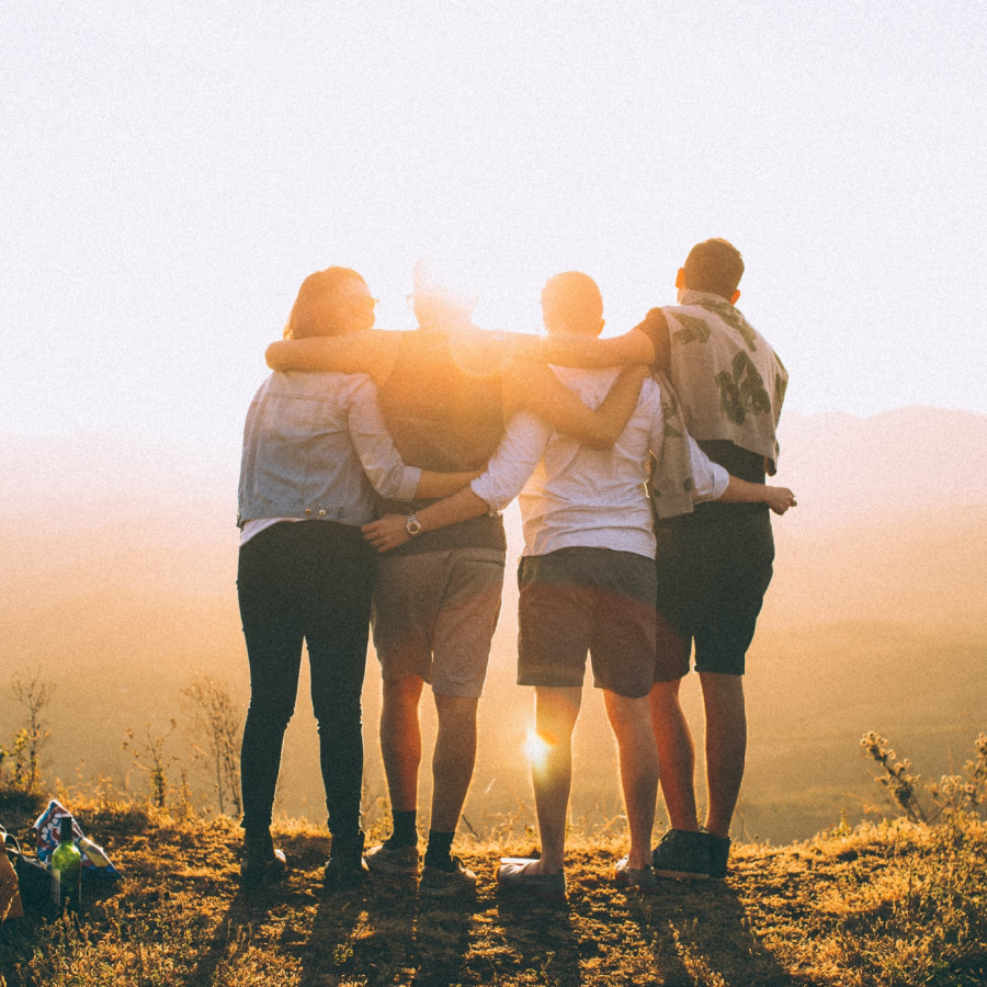 Four people watching the sun rise with their arms around each other