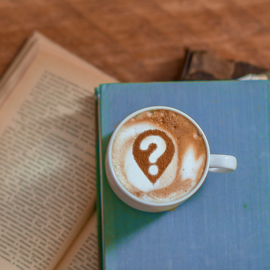 the image of a cup of coffee with a question mark in the foam on top of a blue book within another open book underneath