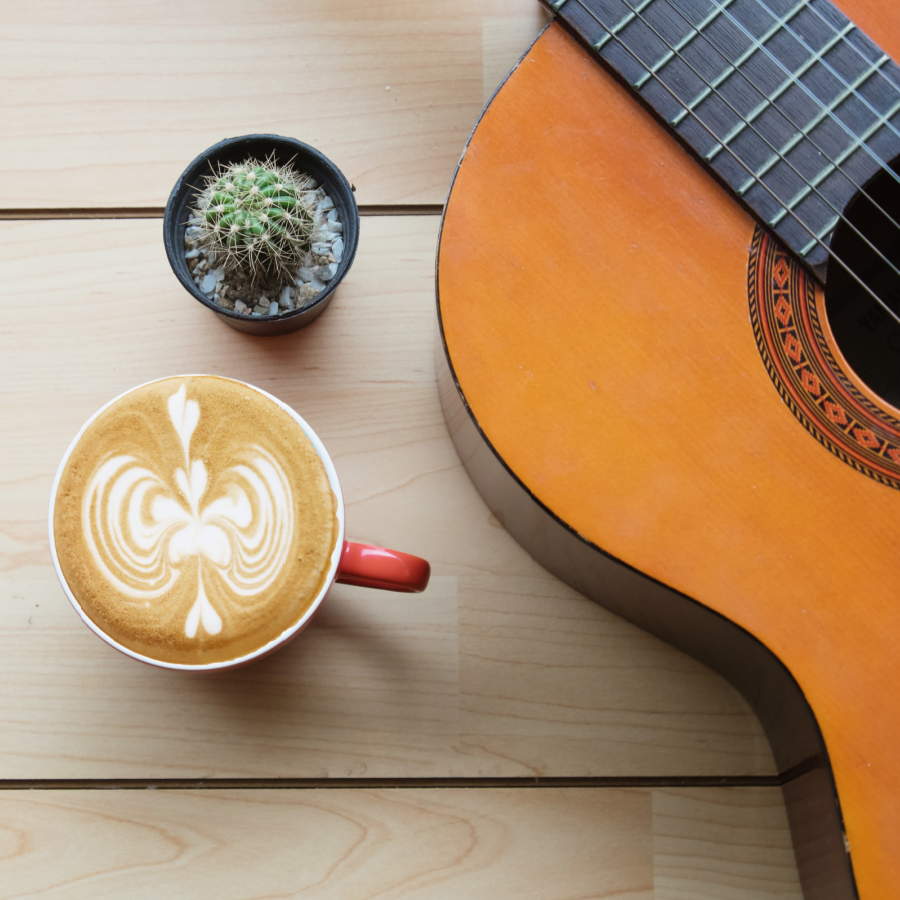 a guitar resting on a wooden table next to a cup of coffee and a cactus plant