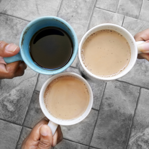 Three hands holding full cups of coffee or tea