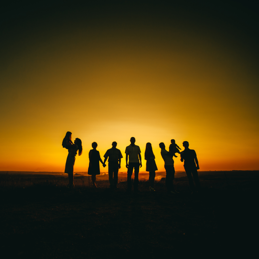 the silhouette of several people of diverse ages in front of a sunset