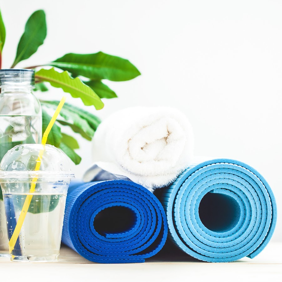 two blue rolled yoga mats, a white towel, a bottle and cup of water, and a green plant